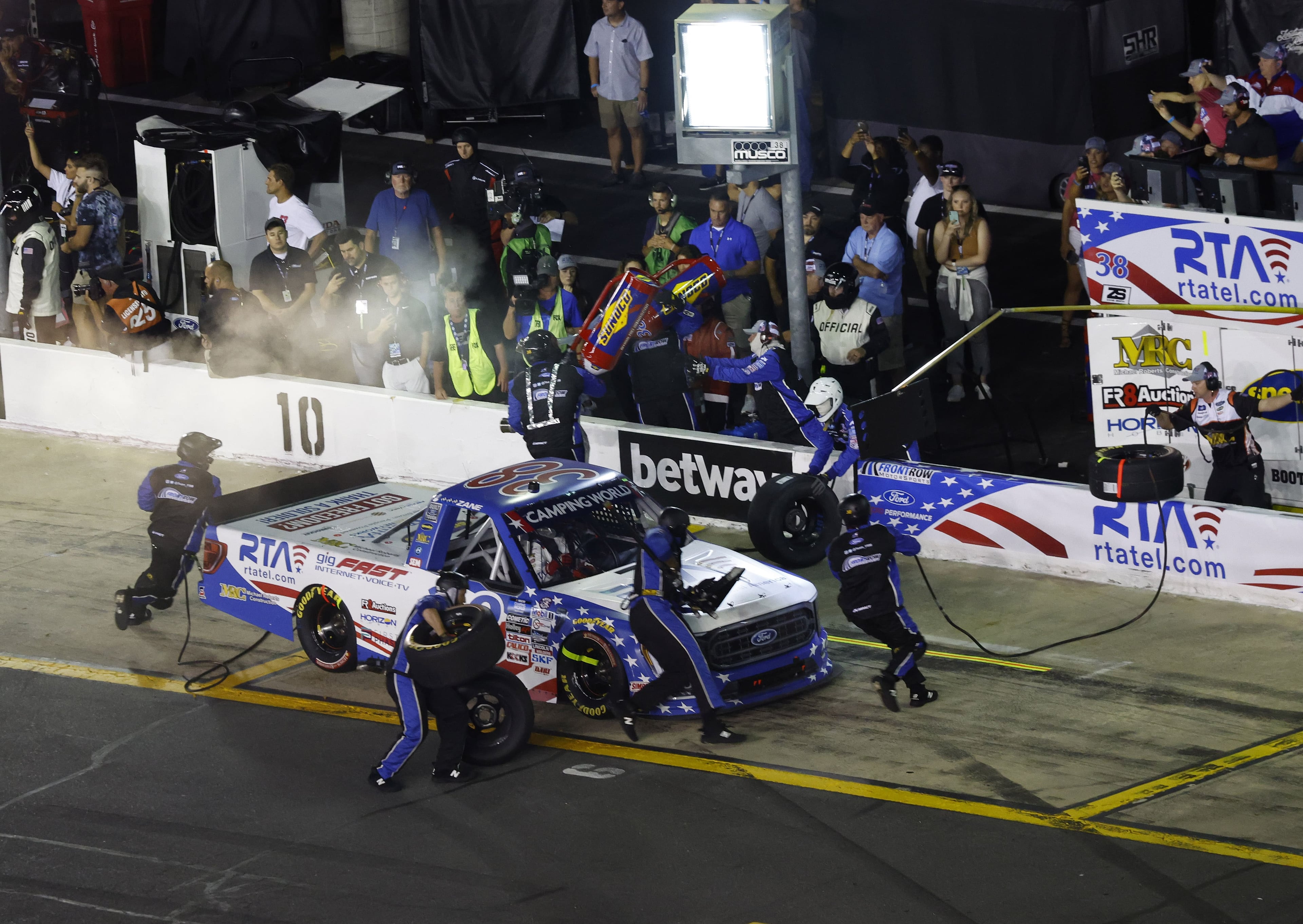 #38 truck during a night pit stop, full crew in action at pit lane