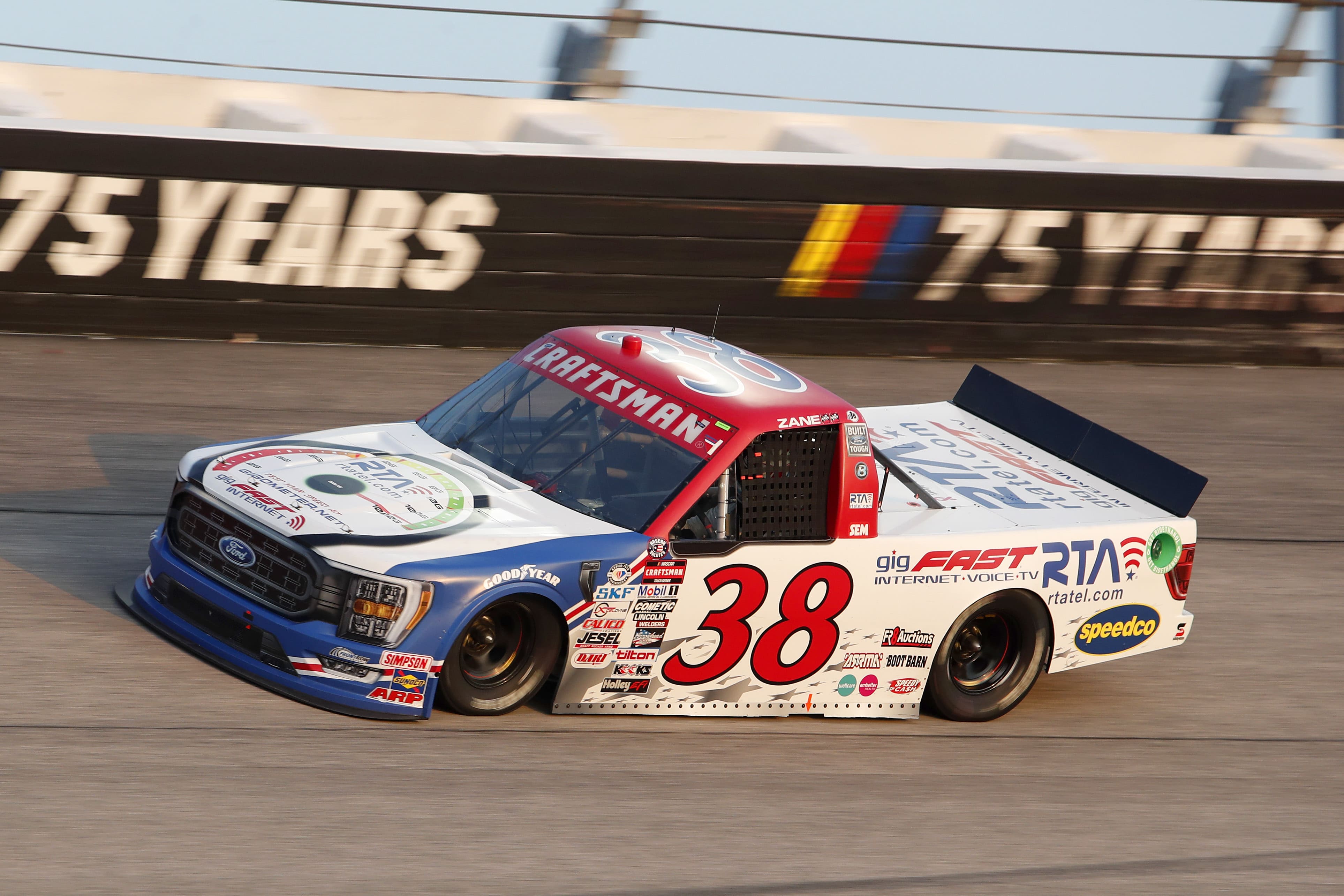 #38 Ford F-150 truck at speed, 75 Years anniversary wall in background