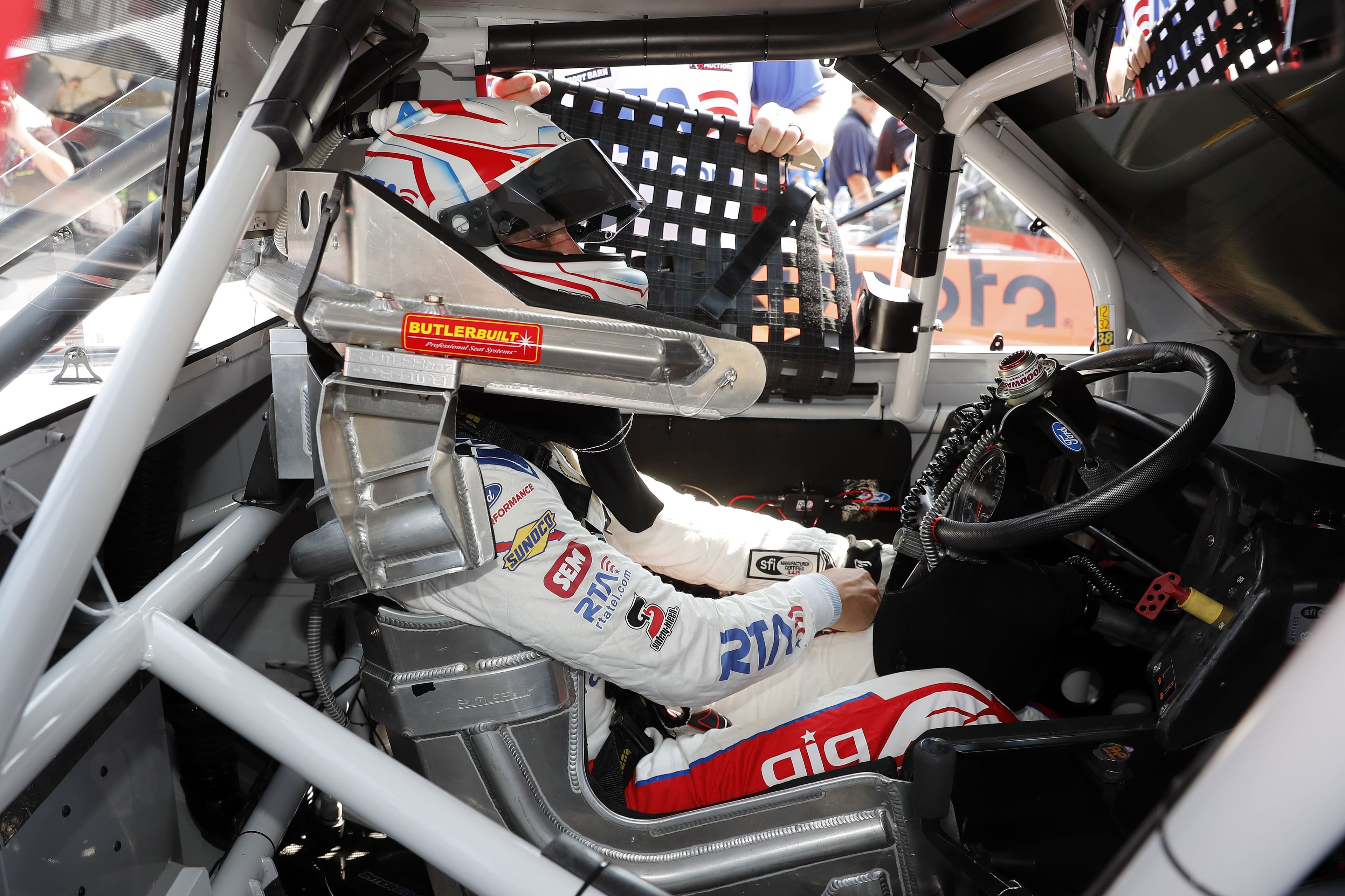 Cockpit interior with Zane Smith in seat wearing helmet, roll cage visible